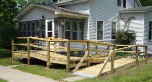 A wooden ramp leading up to the entrance of a white house, providing accessibility for wheelchairs and strollers.